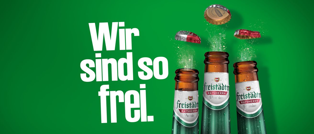 A poster with a green background displays the words 'Wir sind so frei' in bold white letters. It features a bottle of Freistadt Ratsherrn beer with its cap flying off.
