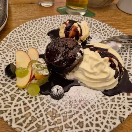A plate with a chocolate cake, ice cream, and fruits, topped with chocolate sauce and powdered sugar.