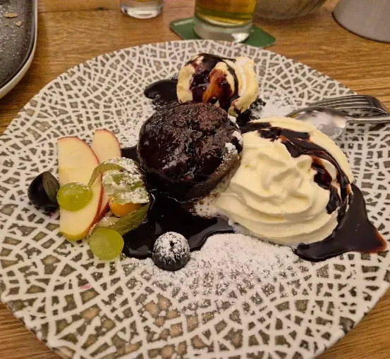 Ein Teller mit einem Schokoladenkuchen, Eis und Früchten, überzogen mit Schokoladensauce und Puderzucker.