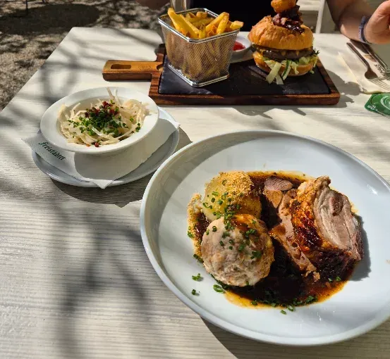 Ein Tisch mit einem Teller Fleisch, Gemüse und einer Beilage Pommes Frites, zusammen mit einer Schüssel Salat und einem Glas Wein.
