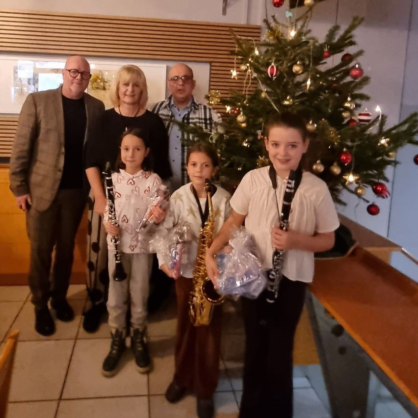 Eine Familie mit drei jungen Mädchen posiert mit ihren Musikinstrumenten, Klarinetten und einer Saxophon, vor einem geschmückten Weihnachtsbaum.