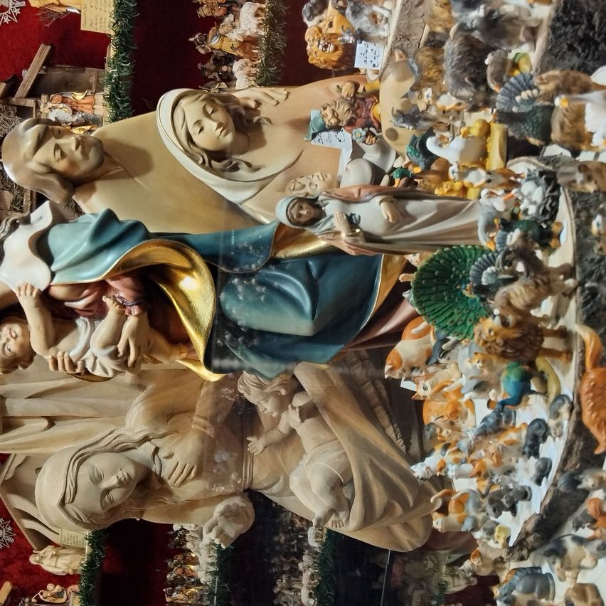 Eine Statue von Maria und Jesus mit einem Säugling, umgeben von verschiedenen Tierfiguren. Die Szene ist mit einem Glasschild bedeckt.