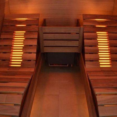 Innenansicht einer Holzsauna mit zwei Bänken, Holzwänden und gelben Lichtern.