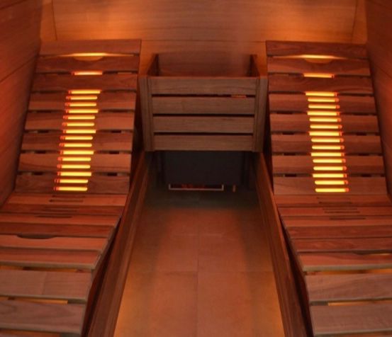 Innenansicht einer Holzsauna mit zwei Bänken, Holzwänden und gelben Lichtern.