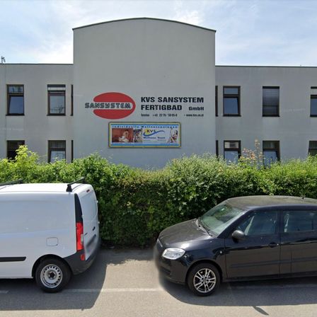 Ein weißer Lieferwagen und ein schwarzer Wagen sind vor einem Gebäude mit dem Namen Sansystem geparkt.