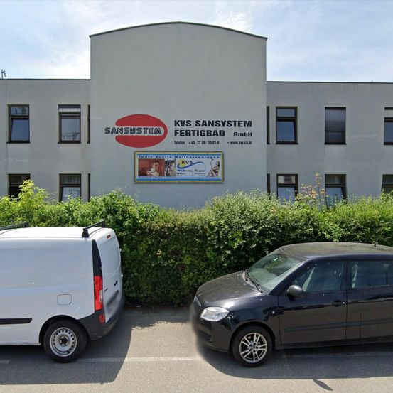 Ein weißer Lieferwagen und ein schwarzer Wagen sind vor einem Gebäude mit dem Namen Sansystem geparkt.