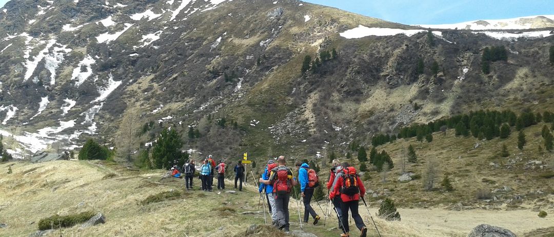 Eine Gruppe von Wanderern mit Rucksäcken und Trekkingstöcken erklimmt einen Berghang unter blauem Himmel mit einzelnen Wolken.
