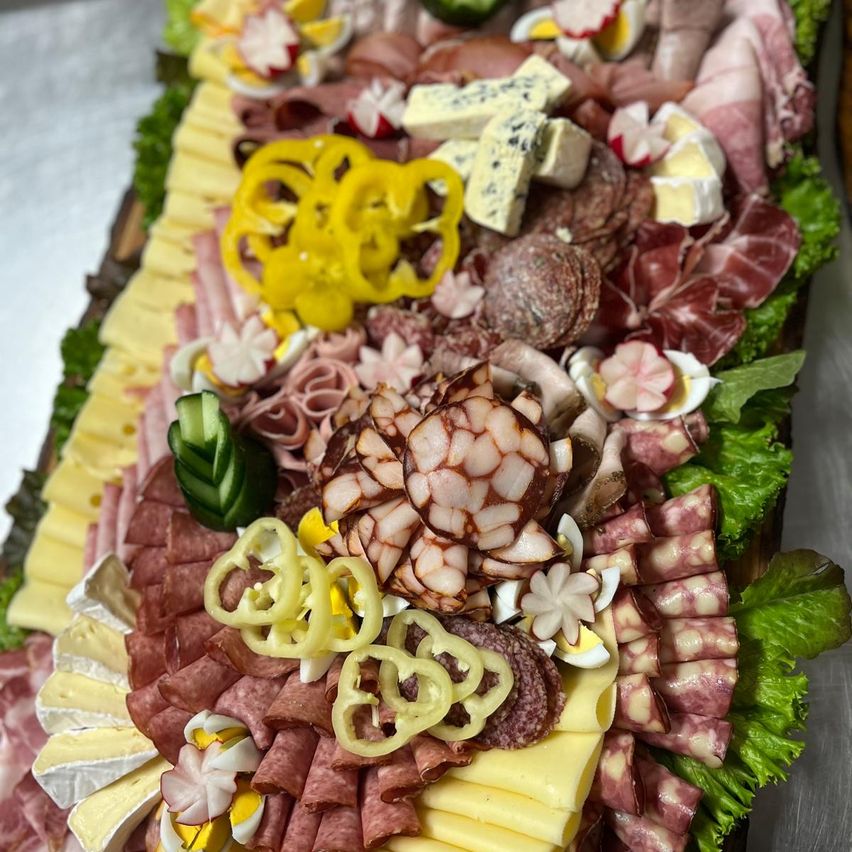 Eine Charcuterie-Platte zeigt eine Auswahl an Fleisch, Käse und Gemüse, mit Blumen und geschnittenen Zitronen als Dekoration.