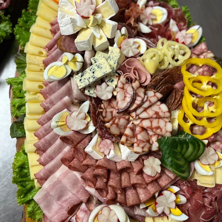 Ein Essensplatter mit einer Auswahl an Fleisch, Käse und Eiern. Die Fleischsorten sind geschnitten und in einer kreisförmigen Form angeordnet. Die Käsesorten sind in kleine Stücke geschnitten und um die Fleischsorten herum angeordnet. Die Eier sind halbiert und auf die Fleischsorten gelegt. Der Platten ist mit blumenförmigen Gemüse garniert.