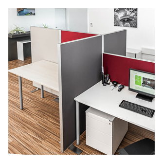 Ein Büroarbeitsplatz mit Schreibtisch, Computermonitor, Tastatur, Maus und anderen Büroartikeln. Der Arbeitsplatz hat eine graue und rote Trennwand. Der Boden ist aus Holz.