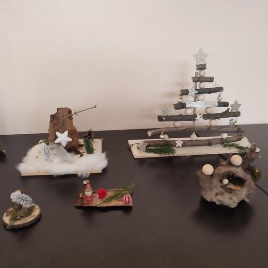 Auf einem dunklen Tisch stehen mehrere handgefertigte hölzerne Weihnachtsdekorationen. Es gibt verschiedene Größen und Stile, einschließlich eines kleinen Gnoms und eines Sterns.