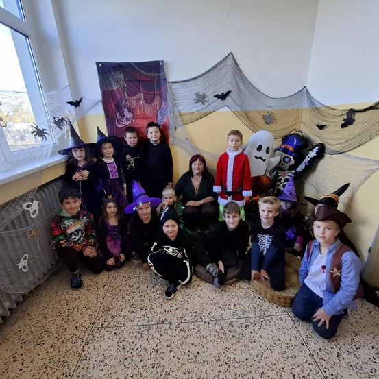 Eine Gruppe von Kindern in verschiedenen Halloween-Kostümen, darunter Hexen, Skelette und der Weihnachtsmann, posiert für ein Foto in einem dekorierten Raum.