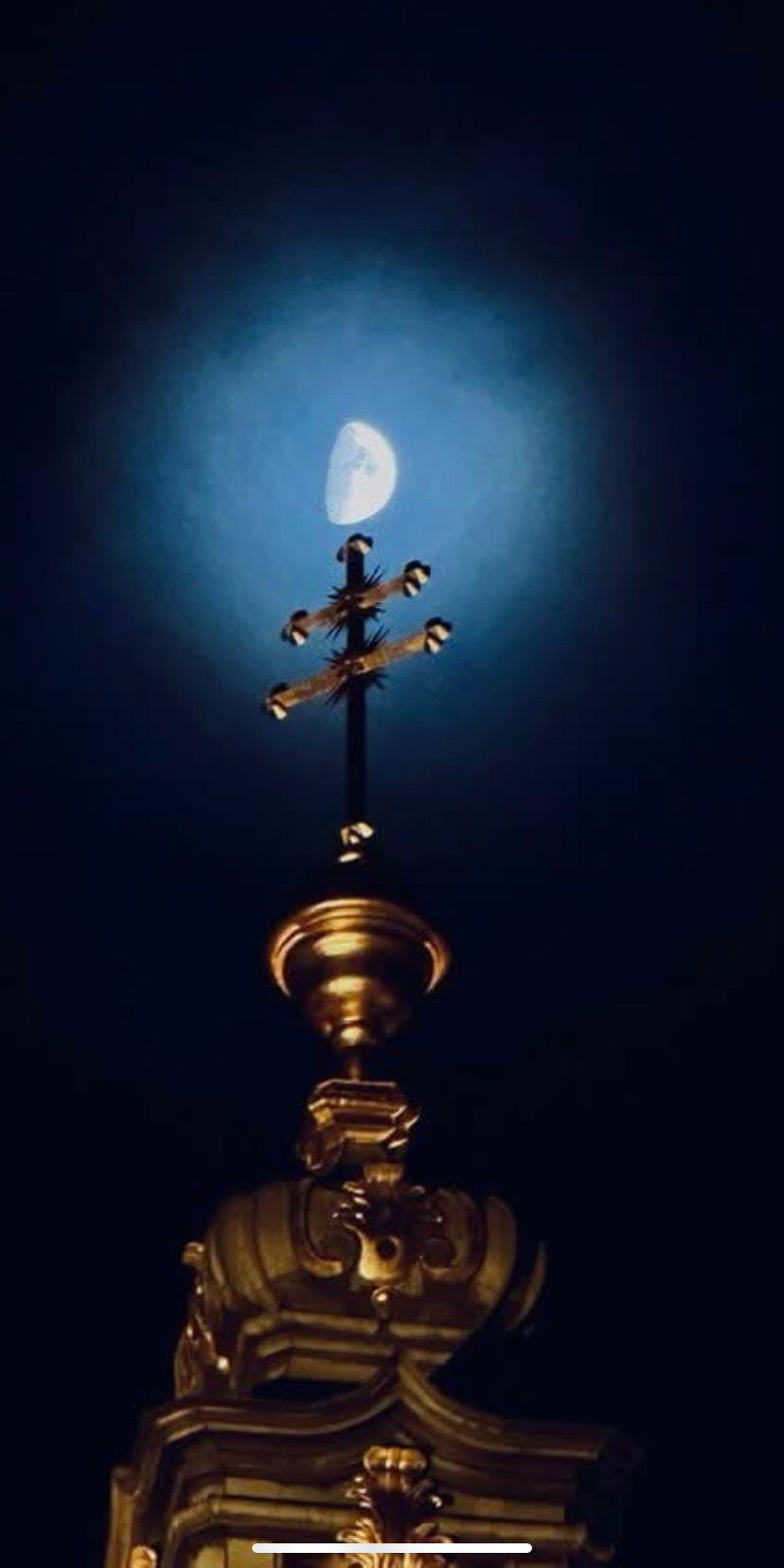 A golden cross stands tall against a dark night sky, with the moon shining brightly above it.