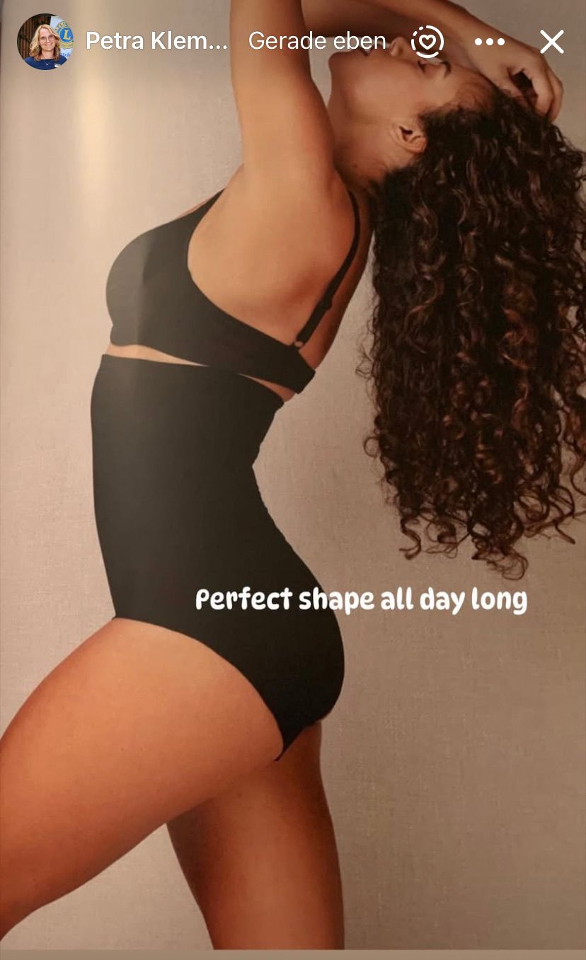 Eine Frau mit lockigem Haar trägt einen schwarzen Einteiler und posiert, um eine perfekte Form den ganzen Tag lang zu zeigen.