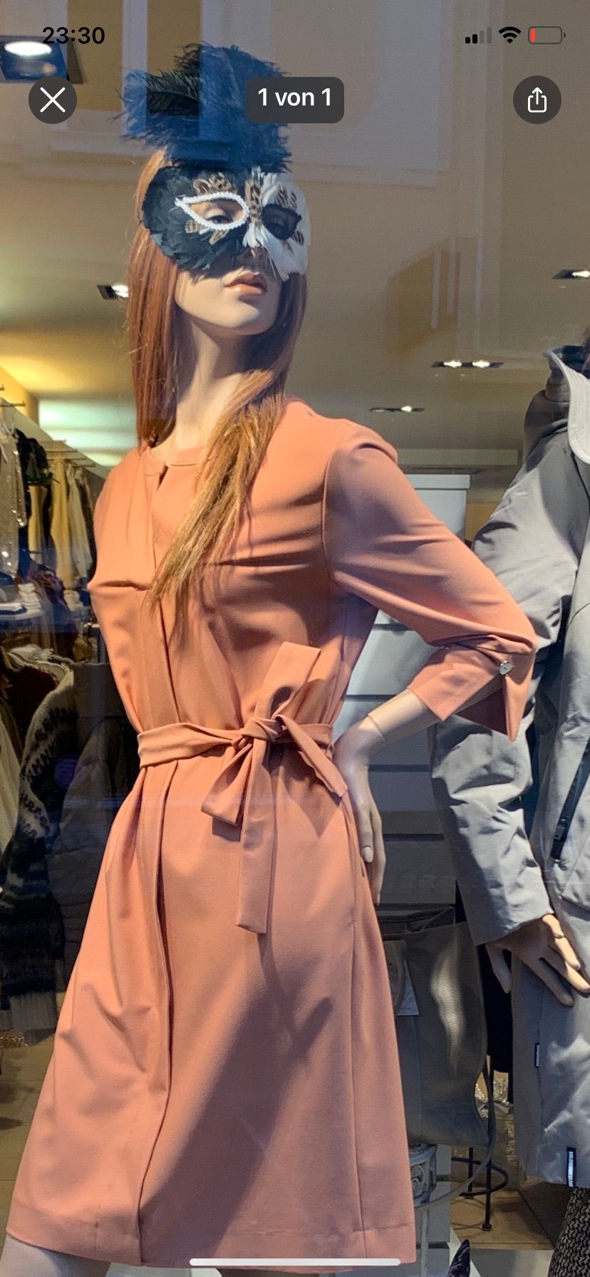 Ein Mannequin zeigt ein pfirsichfarbenes Kleid mit tailliertem Bund und langen Ärmeln in einem Bekleidungsgeschäft.