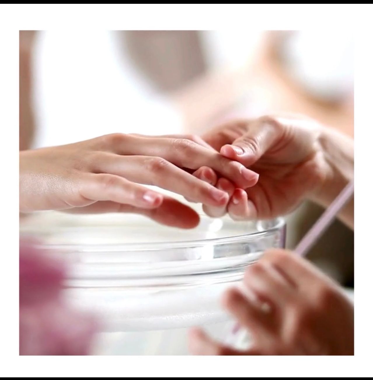 Ein Nahaufnahme einer Hand, die eine Maniküre erhält, wobei die Finger gehalten und poliert werden. Ein Glasbehälter und ein Pinsel sind im Vordergrund sichtbar.