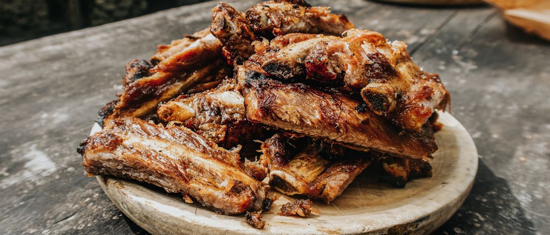 Ein Holzteller mit gegrillten Rippchen. Das Fleisch ist verkohlt und hat einen reichen, rauchigen Geschmack. Es ist eine köstliche und appetitliche Mahlzeit.