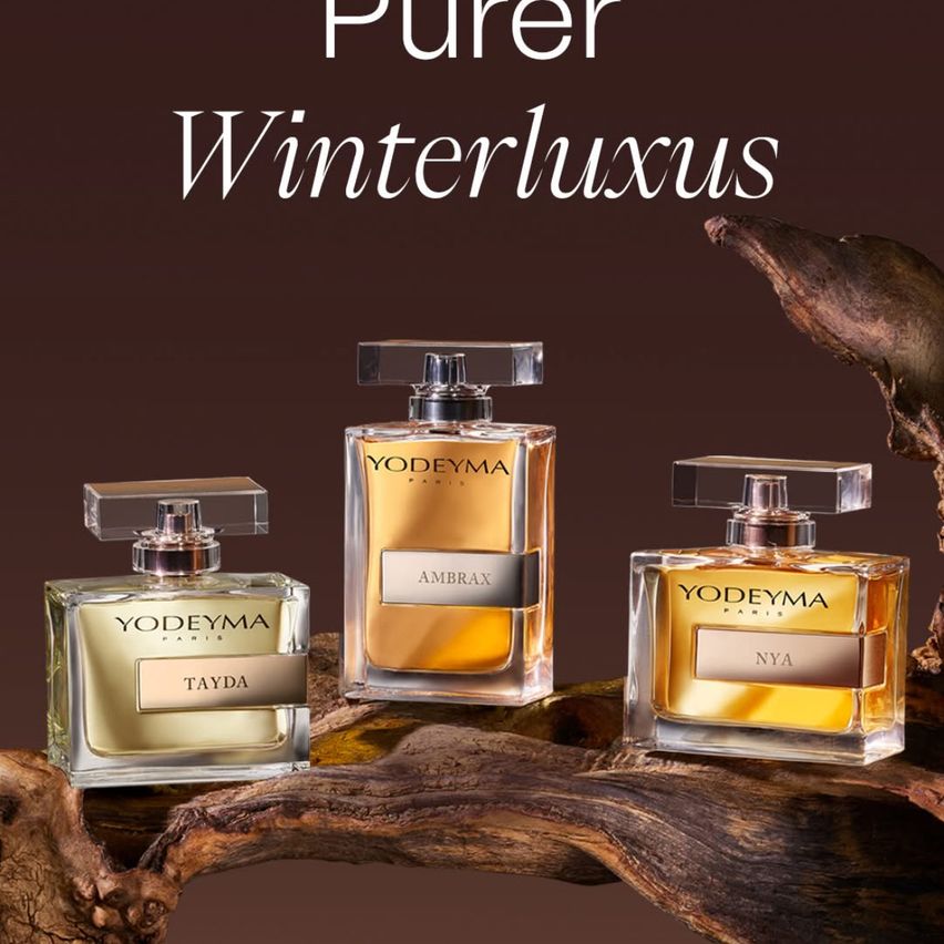 Drei Parfümflaschen sind auf einem Ast ausgestellt. Die Flaschen sind gold und klar, mit Etiketten, die 'YODEYMA PARIS', 'AMBRAX' und 'NYA' lesen. Über den Flaschen steht der Text 'Purer Winterluxus'.