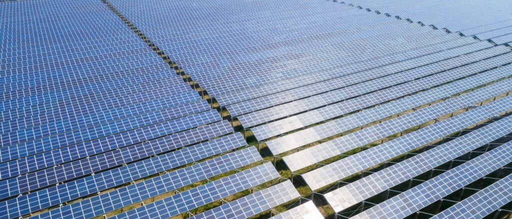 Eine Luftaufnahme eines großen Solarparks mit vielen Reihen von Solarmodulen an einem sonnigen Tag.