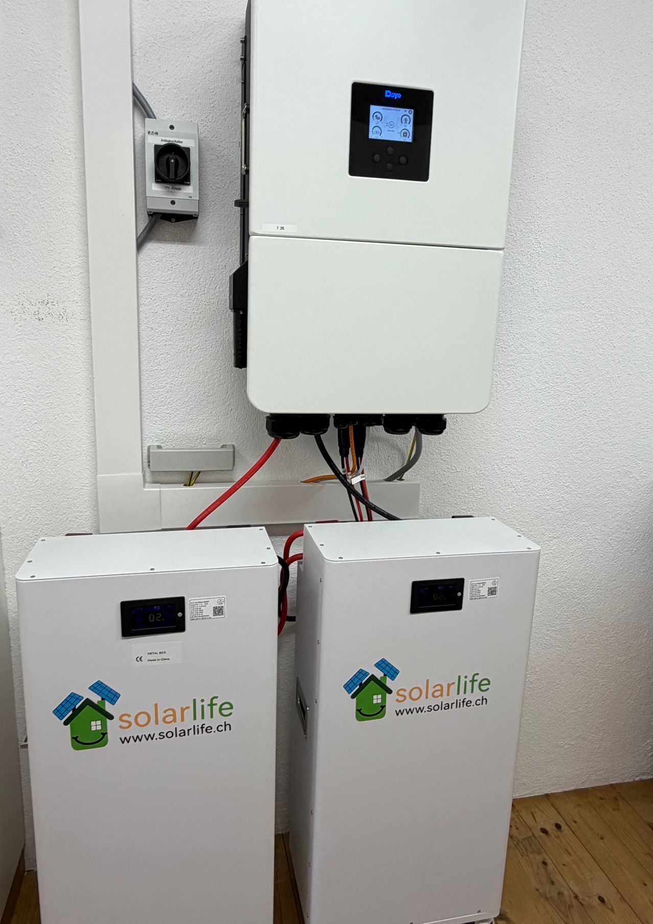 Drei weisse Solarlife-Geräte an einer Wand montiert, mit Kabeln verbunden. Zwei haben Logos und Websites, während das oberste eine digitale Anzeige hat.