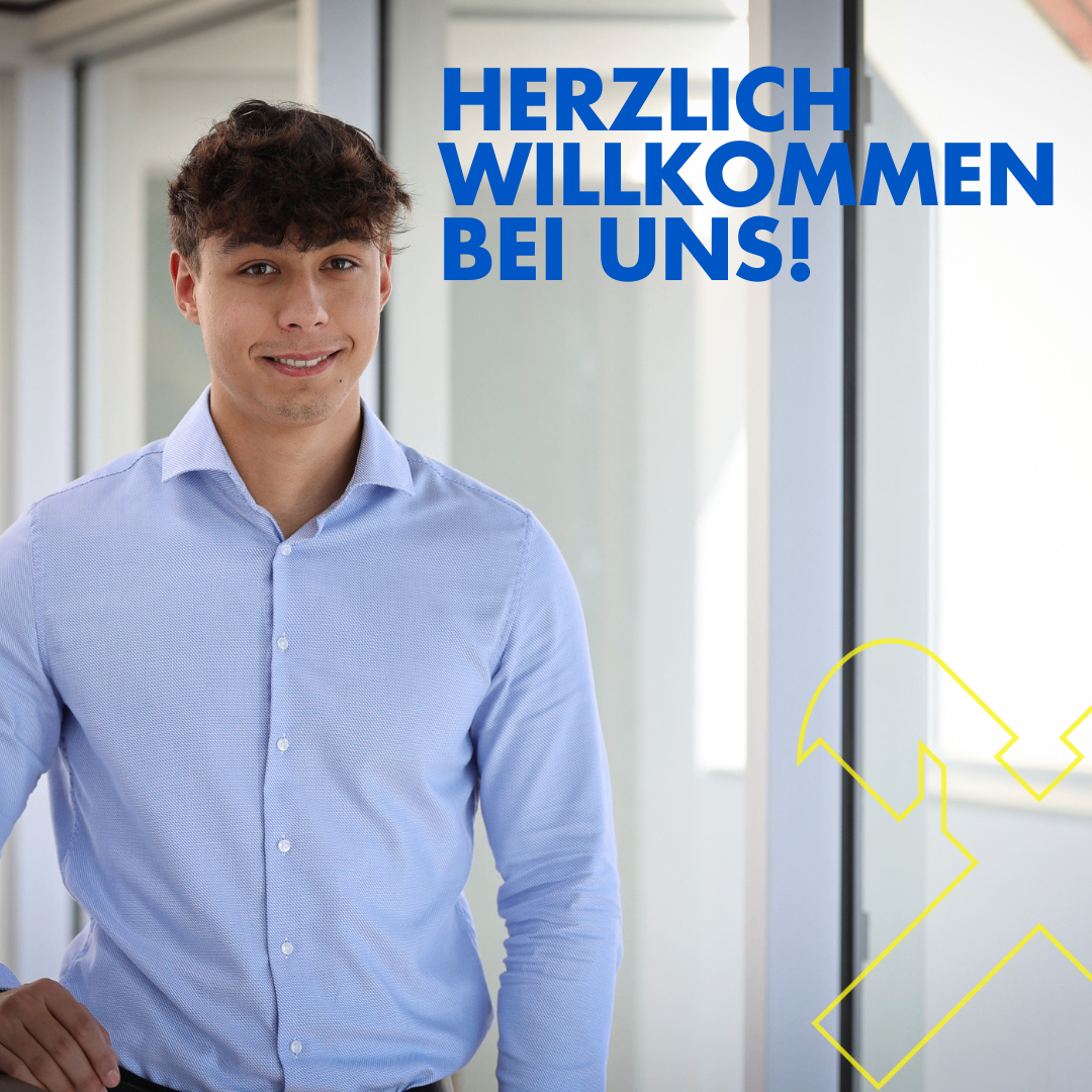 Ein lächelnder Mann in einem hellblauen Hemd steht vor einer Glastür mit den Worten 'Herzlich Willkommen bei uns!' in blauem Text.