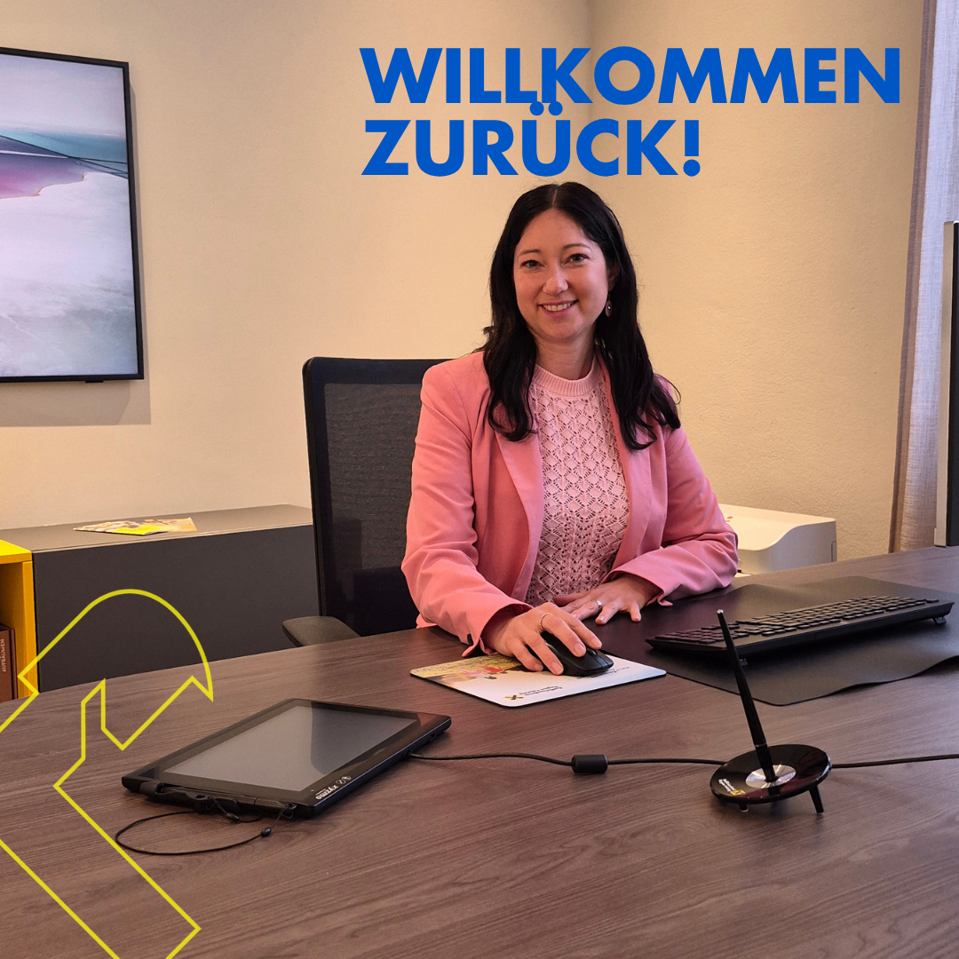 Eine Frau sitzt an einem Schreibtisch mit Computerbildschirm, Tastatur und Maus und lächelt. Die Worte 'Willkommen Zurück!' sind deutlich auf der Wand hinter ihr zu sehen.
