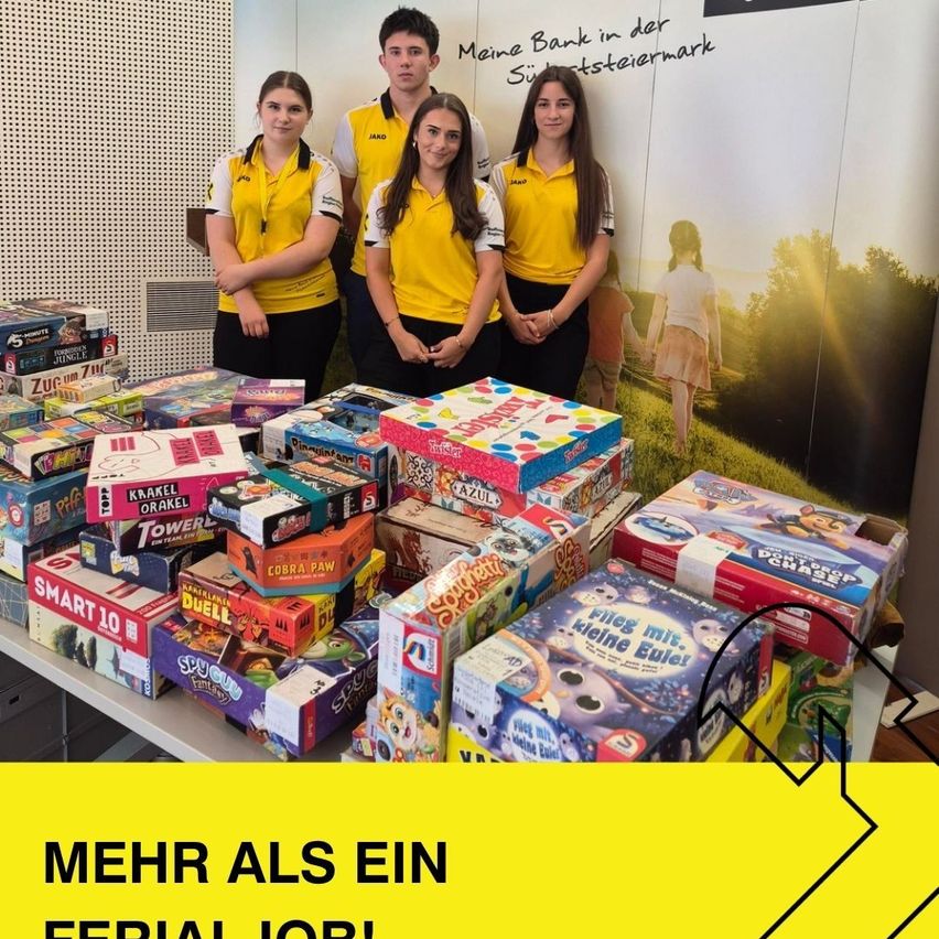 Vier junge Menschen in gelben Uniformen stehen hinter einem Tisch voller verschiedener Brettspiele, mit einem Banner im Hintergrund, das 'Meine Bank in der Steiermark' besagt.