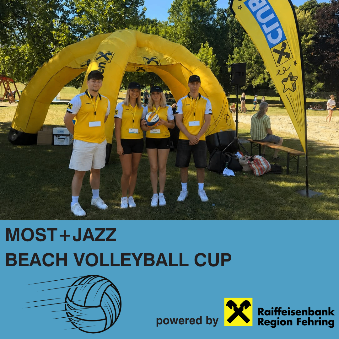 Four people wearing yellow uniforms stand in a yellow tent at a beach volleyball event, with a volleyball in hand. An advertisement banner is behind them.