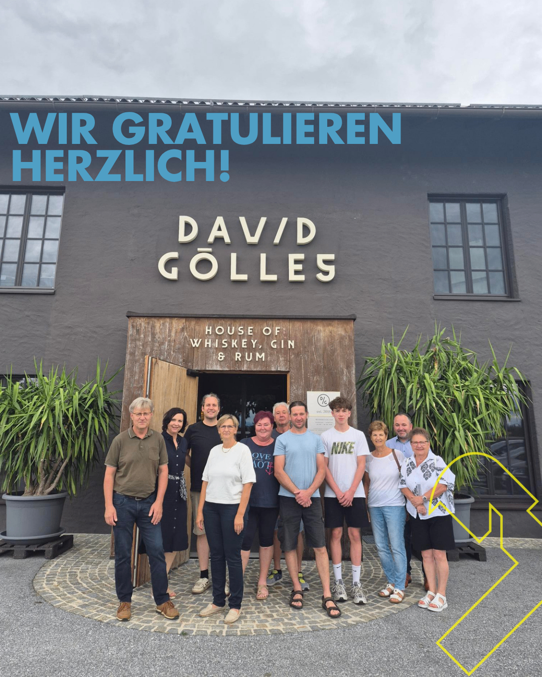 A group of adults stands in front of the DaVd Golles House of Whiskey, Gin, and Rum, with the words Wir Gratulieren Herzlich written above them.