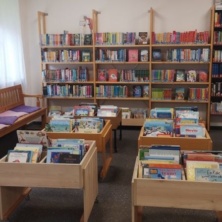 Eine Bibliothek mit bunten Büchern auf Holzregalen und einer Bank mit Kissen.