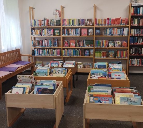 Eine Bibliothek mit bunten Büchern auf Holzregalen und einer Bank mit Kissen.
