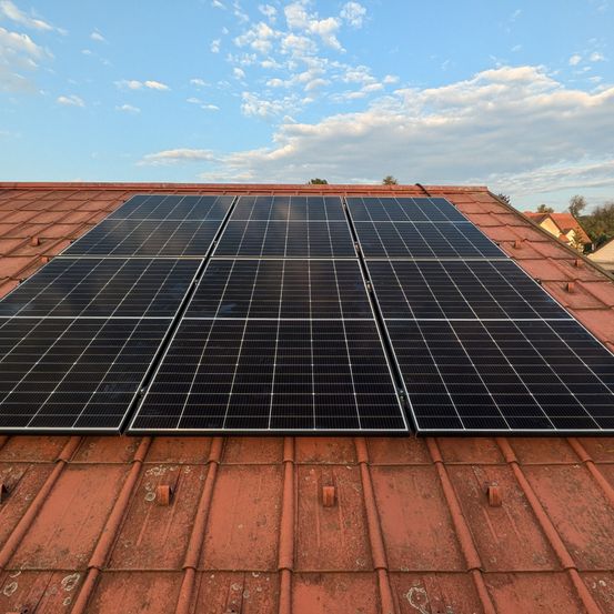 Solarmodule sind auf einem roten Dach unter einem blauen Himmel mit verstreuten Wolken installiert.