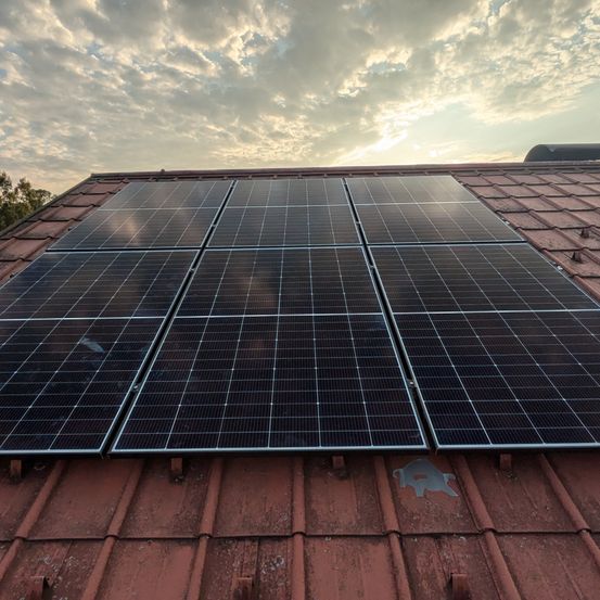 Ein Dach mit mehreren Solarmodulen, die den Himmel und Wolken reflektieren.