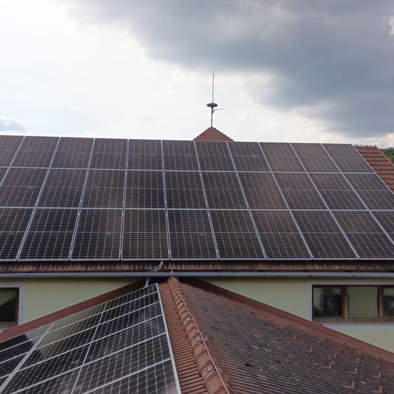 Ein Haus mit Solarpanelen auf dem Dach, unter einem bewölkten Himmel. Die Solarpanele sind ordentlich auf dem Dach angeordnet.
