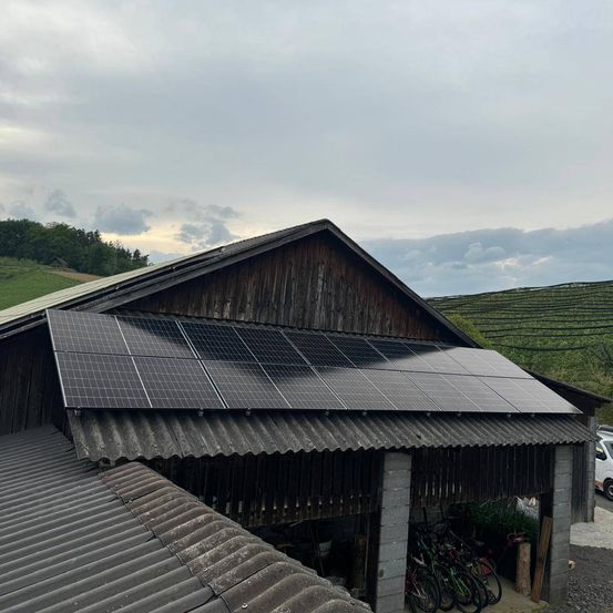 Ein Scheune mit Solarpaneelen auf dem Dach und Fahrrädern, die im Inneren unter einem bewölkten Himmel geparkt sind.