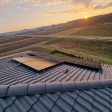 Ein Dach mit Solarpanelen auf einem grauen Dach, mit Blick auf ein weites Feld und eine untergehende Sonne.