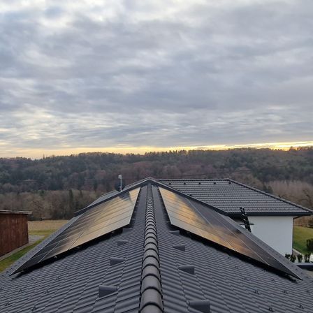 Ein Haus mit Solarpanelen auf dem Dach unter einem bewölkten Himmel mit Bergen im Hintergrund.