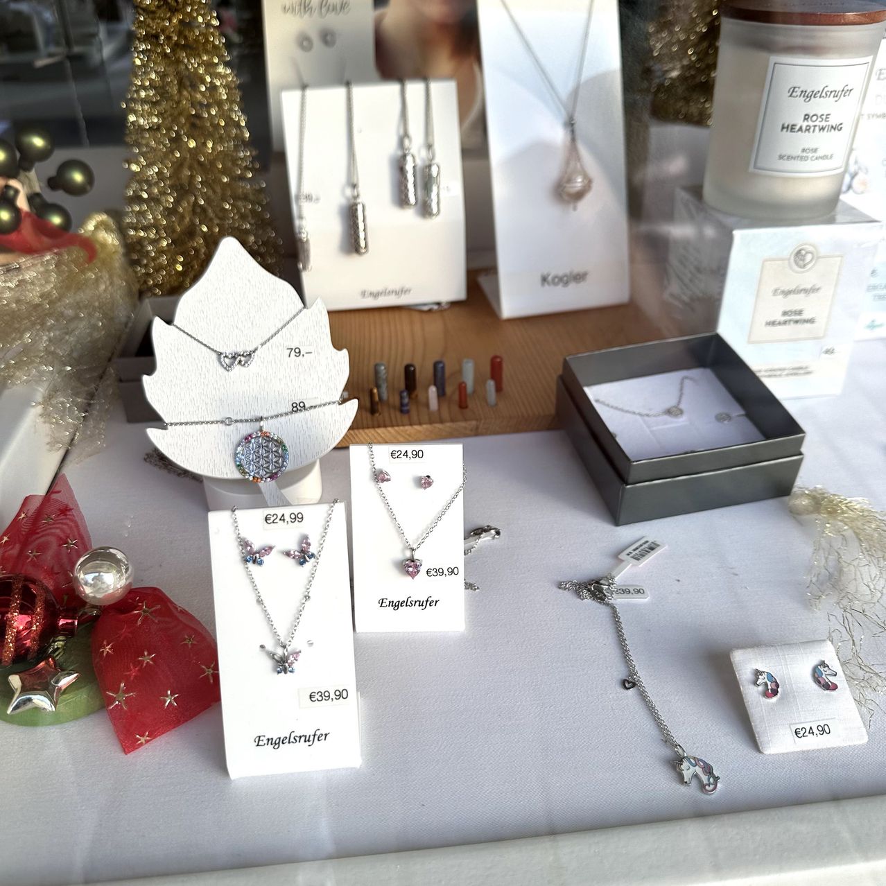 Schmuckdisplay mit verschiedenen Halsketten, Ohrringen und Accessoires. Preisschilder sind sichtbar. Ein Weihnachtsbaum und eine Kerze im Hintergrund.