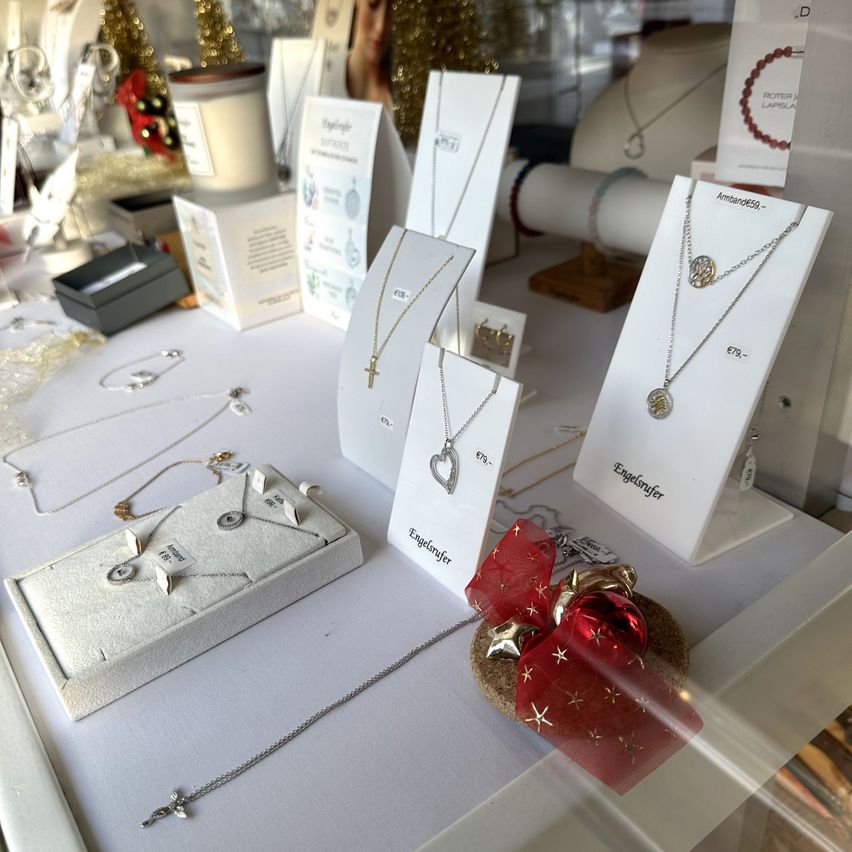 Eine Schmuckausstellung mit verschiedenen Halsketten, Anhängern und Armbändern auf einem weißen Tisch. Es gibt auch Geschenkboxen, eine Kerze und andere dekorative Gegenstände.