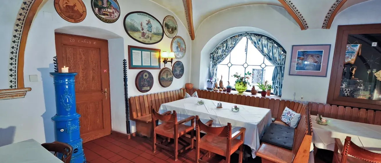 Ein gemütlicher Essbereich mit rotem Fliesenboden und Holzstühlen um einen Tisch. Der Raum verfügt über Holzbänke, dekorative Teller an der Wand und ein Fenster mit Blick auf Pflanzen.