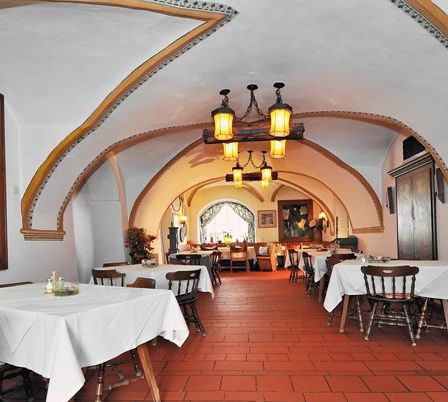 Ein Innenbereich zum Essen mit Holztischen und Stühlen. Die Wände sind weiß und der Boden besteht aus roten Ziegeln. An der Decke hängen Lampen. Ein Gemälde mit schwarz-weißem Design ist an der Wand montiert.