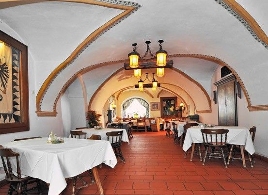 Ein Innenbereich zum Essen mit Holztischen und Stühlen. Die Wände sind weiß und der Boden besteht aus roten Ziegeln. An der Decke hängen Lampen. Ein Gemälde mit schwarz-weißem Design ist an der Wand montiert.