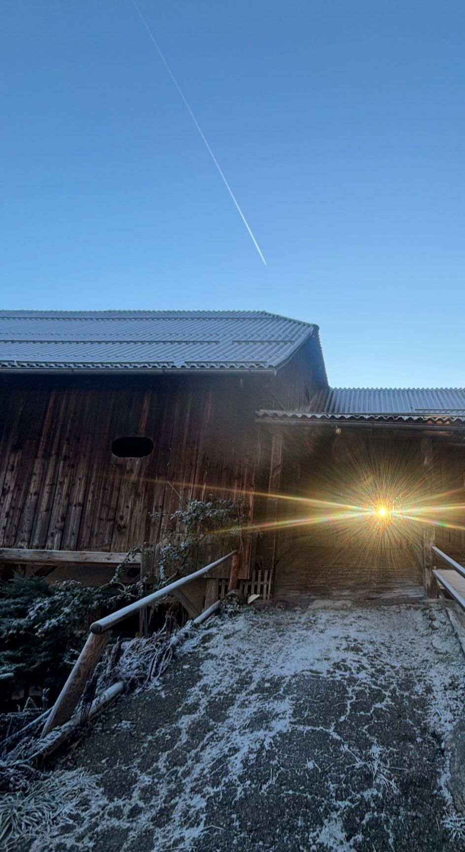 Ein Bauernhaus mit Metalldach und Holzwänden. Sonnenlicht scheint durch ein Loch in der Wand und wirft Strahlen auf den schneebedeckten Boden.