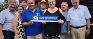 Eine Gruppe von Menschen steht unter einem Zelt, lächelt und posiert für ein Foto. Ein Mann in einem blauen Shirt hält ein blaues Banner mit dem Text 'NOJ Wartmannstetten'.
