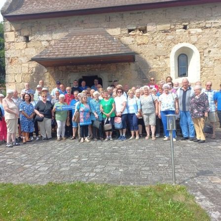 Eine Gruppe von Menschen, gekleidet in verschiedene Sommerkleidung, posiert für ein Foto vor einem alten Steingebäude mit Fenster und Tür.