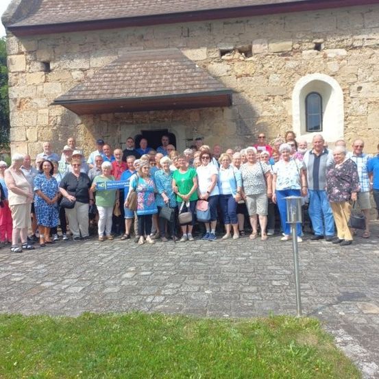 Eine Gruppe von Menschen, gekleidet in verschiedene Sommerkleidung, posiert für ein Foto vor einem alten Steingebäude mit Fenster und Tür.