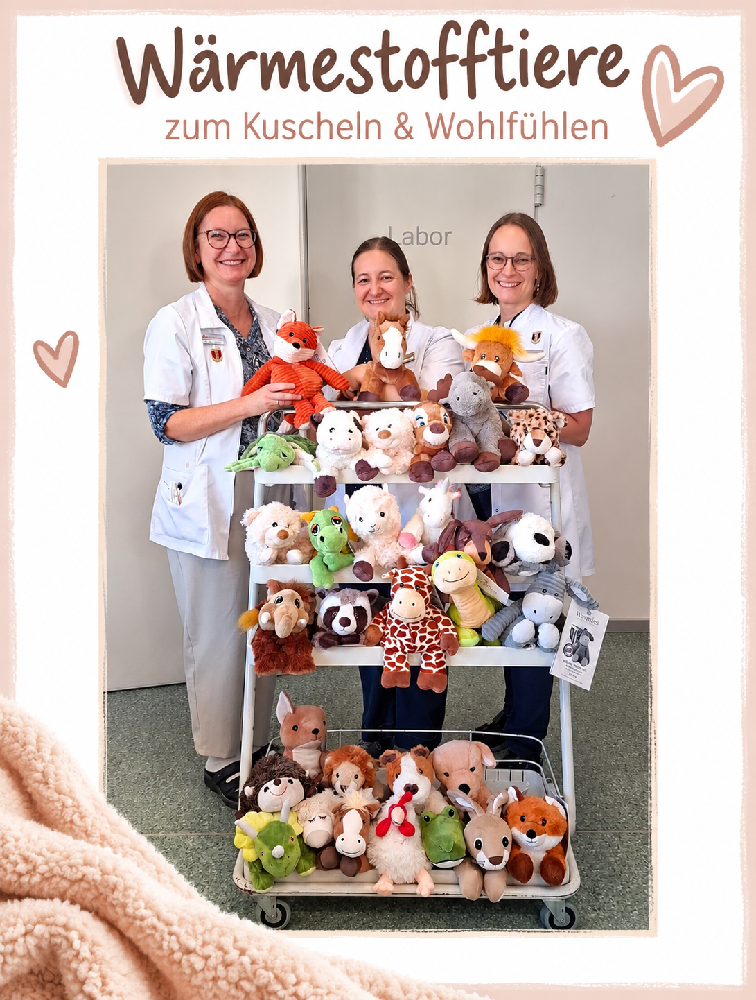 Drei Frauen in weißen Laborkittel stehen hinter einem Wagen voller Kuscheltiere.