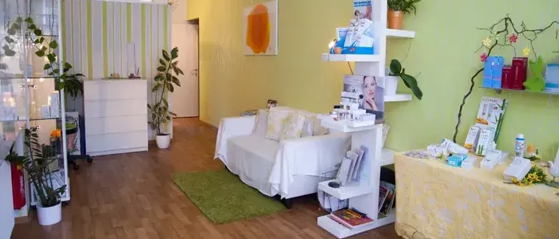 Ein Raum mit einer weißen Couch, einem grünen Teppich und Regalen mit Pflanzen und Büchern. Die Wände sind gelb gestrichen.