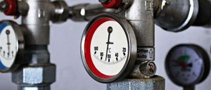 Eine Nahaufnahme eines Metalldruckmessers mit einem roten und weißen Gesicht, das einen Temperaturbereich von 20 bis 100 Grad Celsius zeigt. Der Messing ist an einem Ventilsystem befestigt.