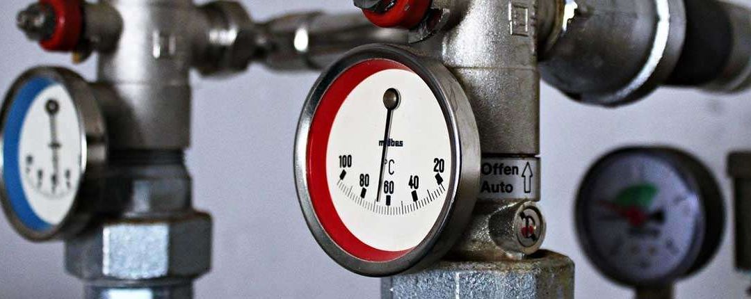 Eine Nahaufnahme eines Metalldruckmessers mit einem roten und weißen Gesicht, das einen Temperaturbereich von 20 bis 100 Grad Celsius zeigt. Der Messing ist an einem Ventilsystem befestigt.